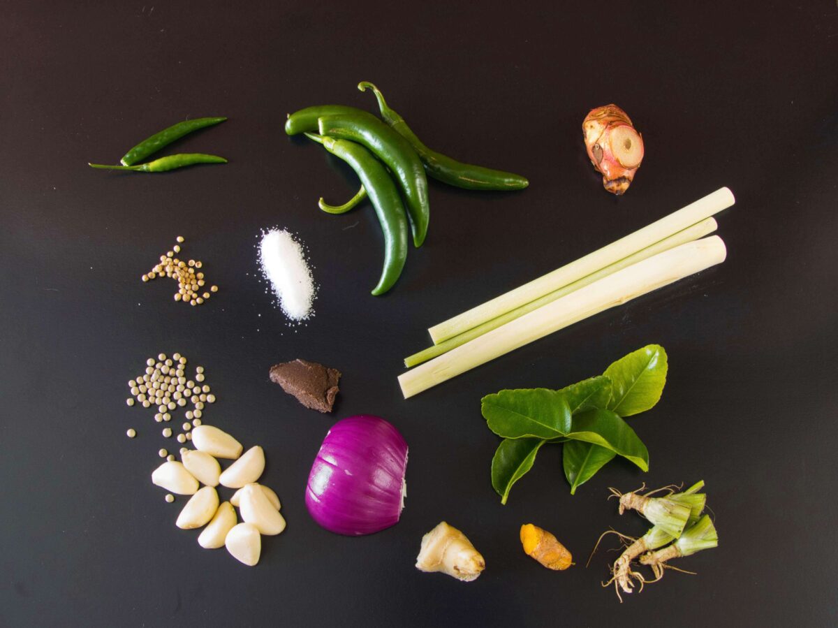 Fresh ingredients for Thai green curry paste, including lemongrass, galangal, kaffir lime, garlic, shallots, green chilies, and coriander roots.