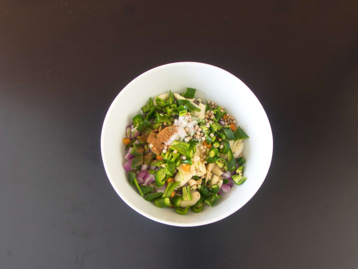 Freshly chopped ingredients for Thai green curry paste, including lemongrass, galangal, kaffir lime zest, garlic, shallots, and green chilies, ready to be ground in a mortar and pestle