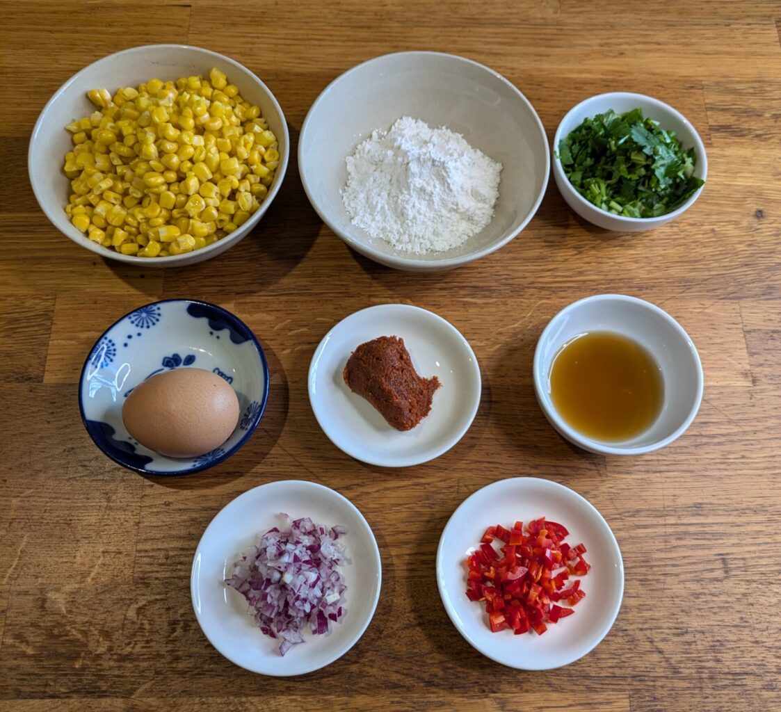 “Ingredients for Thai corn fritters including corn, curry paste, herbs, and flour.”