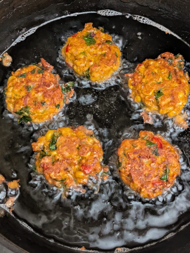 “Golden Thai corn fritters frying in a hot pan.”