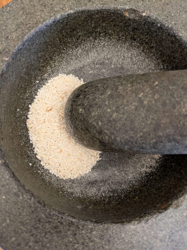 "Toasted rice being ground in a mortar and pestle to create coarse toasted rice powder for salads and laab."