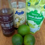 Fresh limes, bottled lime juice, fish sauce, and sesame oil arranged on a kitchen bench for making Thai laab dressing.