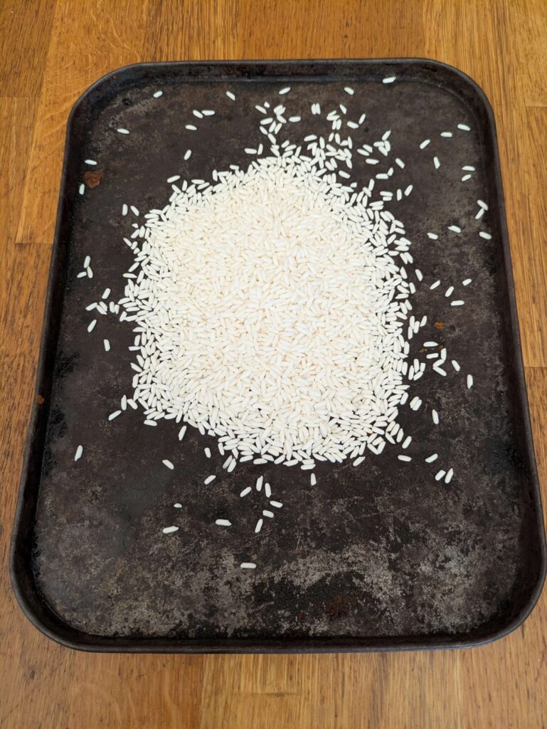 "Uncooked glutinous rice spread evenly on a tray, ready to be dry-toasted for making toasted rice powder."