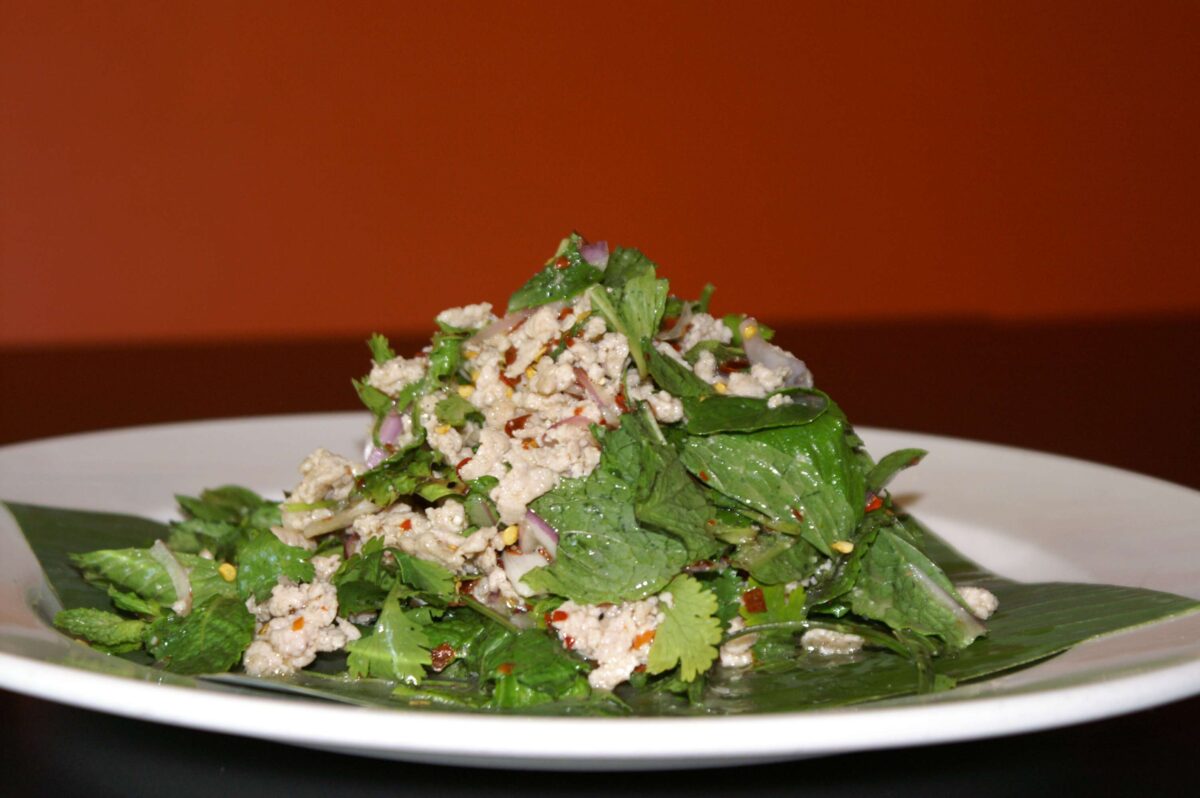 Thai chicken laab served on a plate with fresh herbs, toasted rice, and chilli flakes