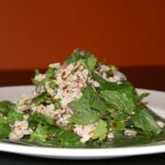 Thai chicken laab served on a plate with fresh herbs, toasted rice, and chilli flakes