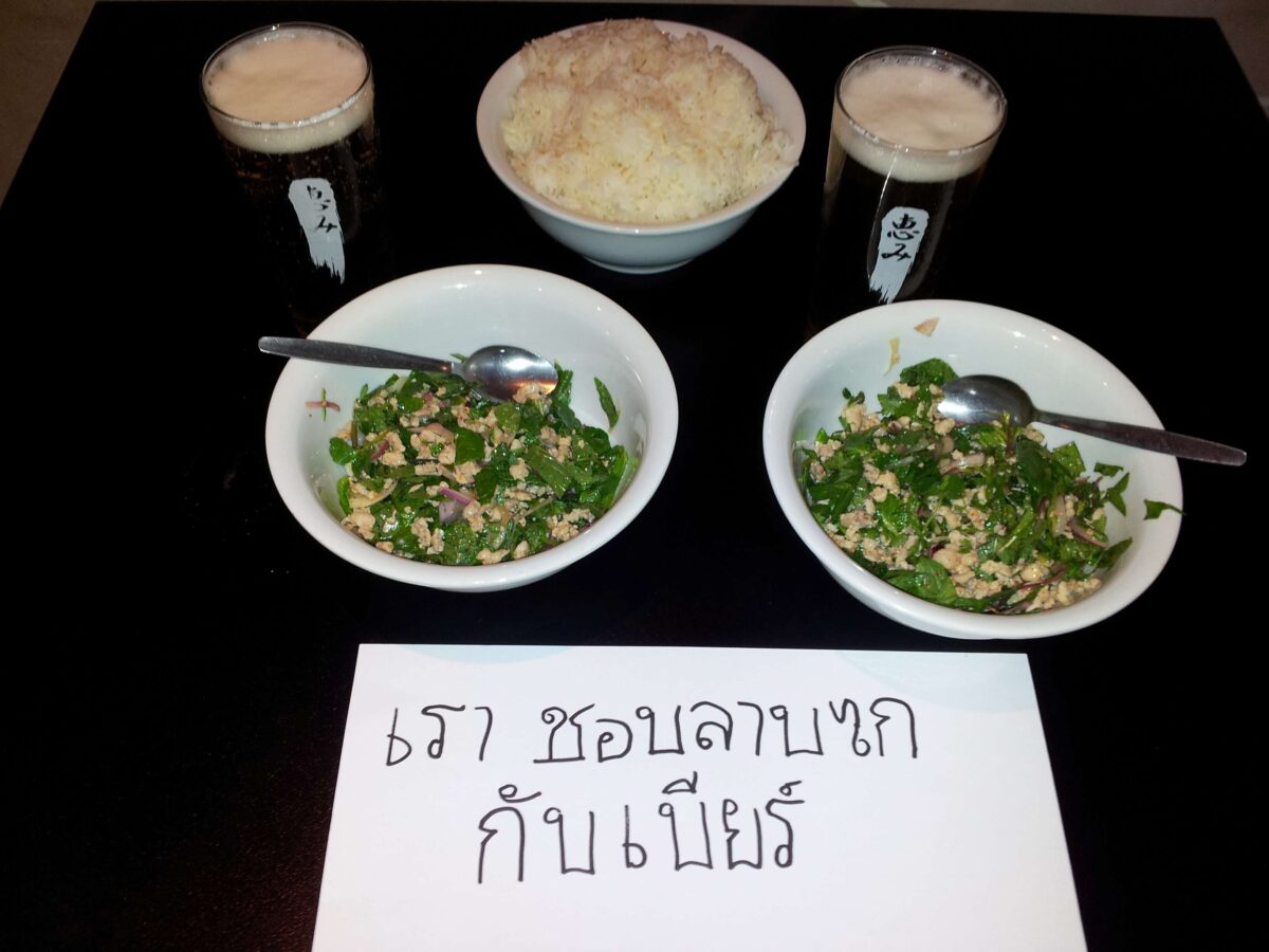 A staff meal favourite: Thai chicken laab served with cold beer and a handwritten sign reading “We love laab gai with beer,” capturing the simple pleasures of life in the kitchen after service.