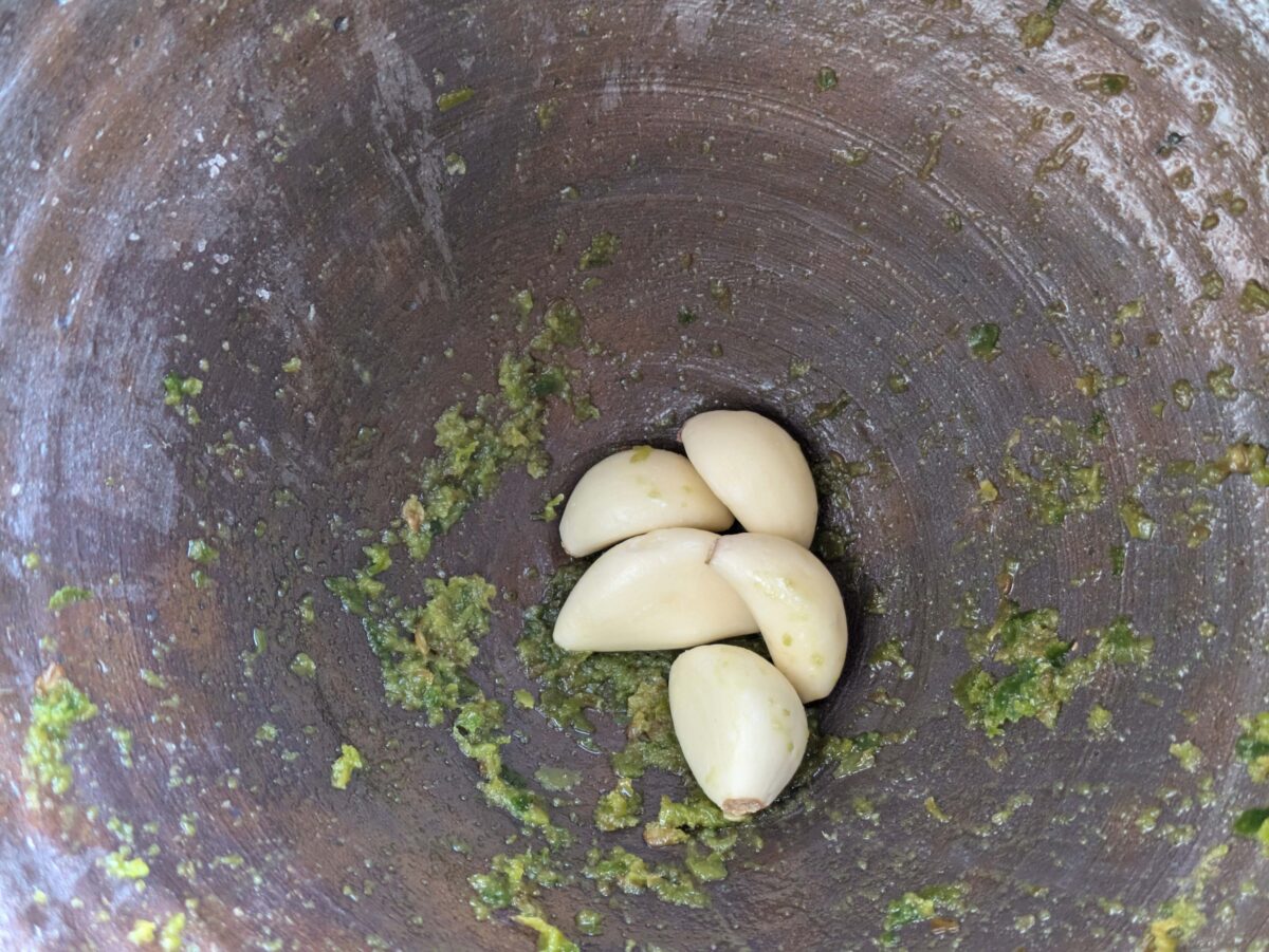 Whole garlic cloves added to ground green chillies and salt in a mortar for Thai chilli dressing